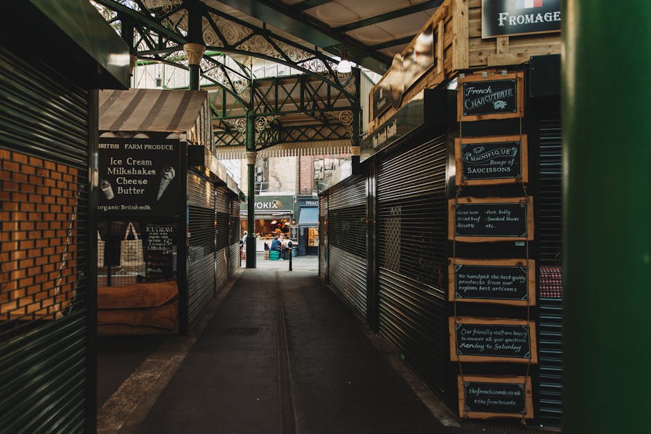 A display of intricately patterned, woven carpets laid out on tables at Brixton Market, with vibrant colors and detailed floral and medallion designs. The carpets' surfaces appear clean and well-maint